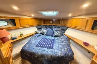 Cozy bedroom in 1989 Fairline 50 yacht with blue bedding and wooden cabinets.