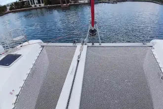 Catamaran Lagoon 42 (2020) with netting over water, docked in a serene marina.