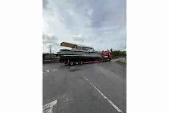 2025 Linssen 45 SL Sedan yacht on trailer, transported by red truck under cloudy sky.