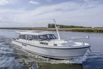 2025 Linssen 45 SL Sedan cruising on a serene waterway under a clear sky.