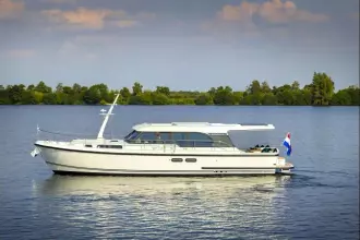 2025 Linssen 45 SL Sedan yacht cruising on a serene lake with lush greenery.